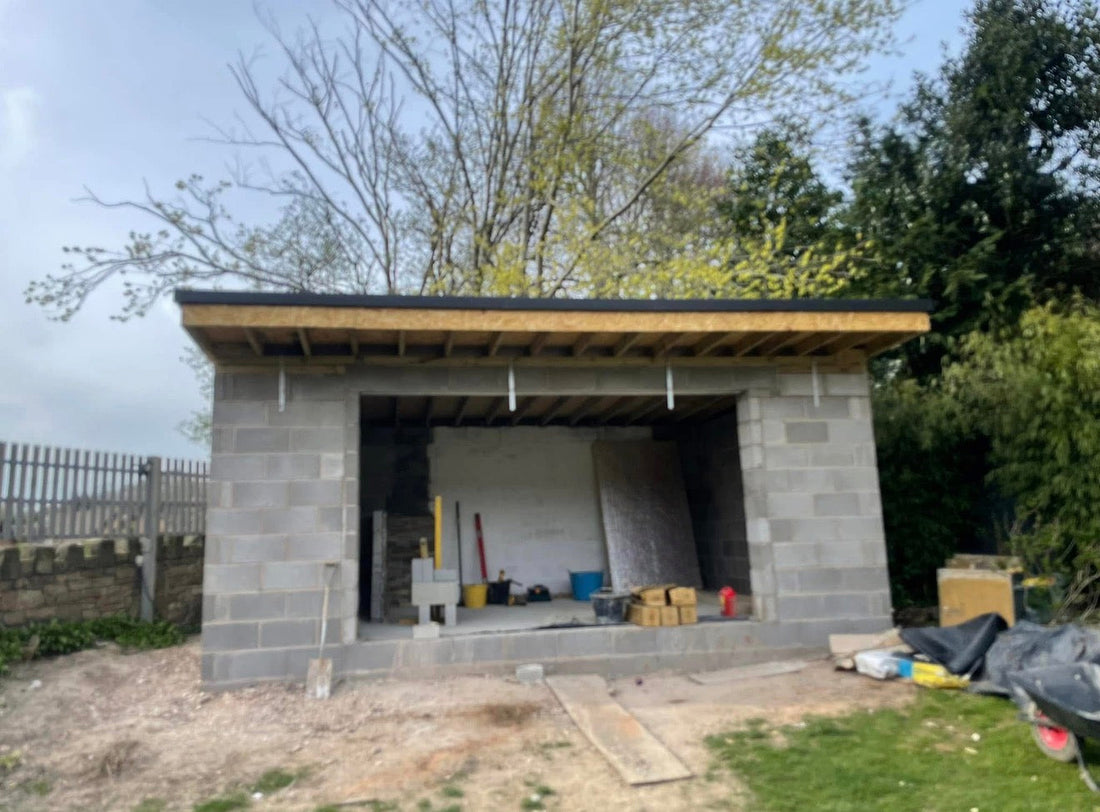 Completed garden bar building in Bolton Lancashire with black EPDM rubber flat roof, timber fascia boards and blockwork walls, front elevation view with garden behind